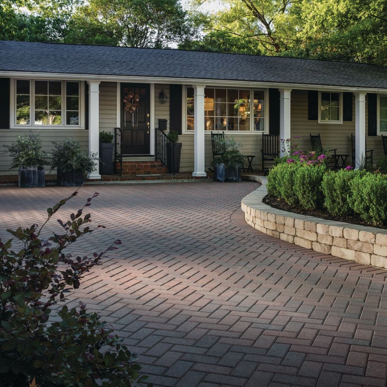 Herringbone-pattern paver driveway with a contrasting soldier-course border curving past a block planter wall — Daedalus Contracting, Lower Mainland BC
